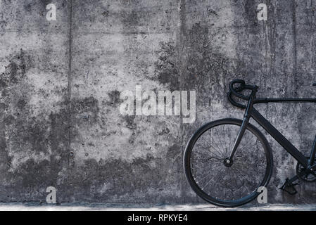 Schwarz-weiß Bild von Fahrrad vor großen Betonwand. Urban Style. Das Fahrrad ist an die Wand gelehnt Stockfoto