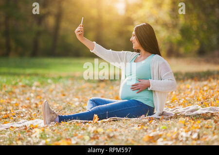 Schwangere Frau im Park. Sie nimmt sich selfie. Stockfoto