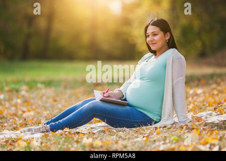 Schwangere Frau im Park. Sie schreibt, um Liste zu tun. Stockfoto
