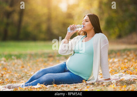 Schwangere Frau im Park. Sie ist Trinkwasser. Stockfoto