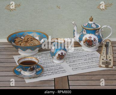 Englisch Teetasse mit Untertasse, Teekanne, creme Kanne und einem Kuchen Schüssel mit Cookies, Fine Bone China Porzellan, und ein Metronom für Musik auf einem Blatt von Musik Stockfoto