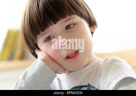 Junge sitzt auf einem Stuhl und seinen Kopf auf seinen Arm Stockfoto