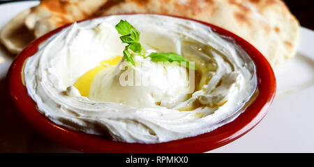 Eine Schüssel cremiges Labneh, ein dicker libanesischer Joghurt-Dip mit Minzblättern und Olivenöl. Nahaufnahme der traditionellen libanesischen Küche in einem Restaurant. Stockfoto