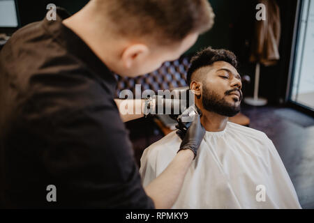 Close up Mann mit Bart Client im barbershop Friseur Friseur auf elektrische Rasierer rasieren. Stockfoto