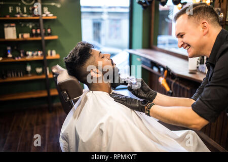 Close up Mann mit Bart Client im barbershop Friseur Friseur auf elektrische Rasierer rasieren. Stockfoto