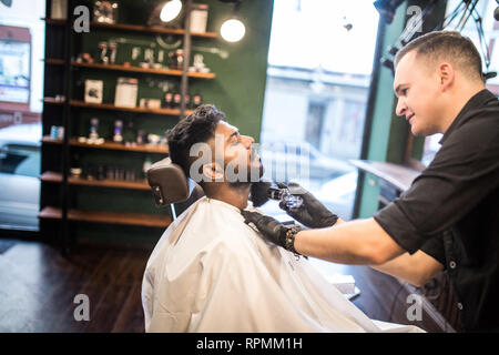 Close up Mann mit Bart Client im barbershop Friseur Friseur auf elektrische Rasierer rasieren. Stockfoto