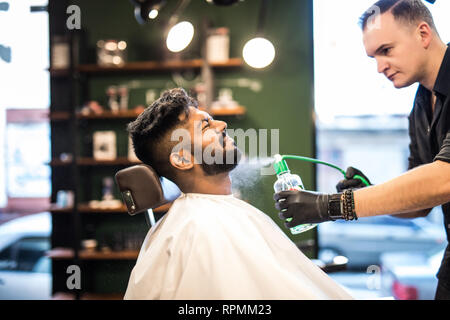 Lächelnd bärtigen Friseur Haare kämmen und Spritzen von Little kid Stockfoto