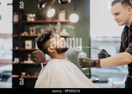 Lächelnd bärtigen Friseur Haare kämmen und Spritzen von Little kid Stockfoto