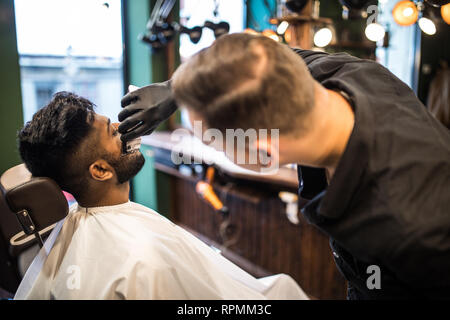 Pflege von echten Menschen. Seitenansicht junger bärtiger Mann, Bart Frisur bei Friseur im Stuhl sitzen im barbershop Stockfoto