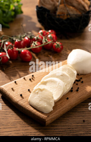 Mozzarella auf Holz Schneidebrett. Kirsche Tomaten im Hintergrund. Holztisch mit Italienischem essen Zusammensetzung Stockfoto