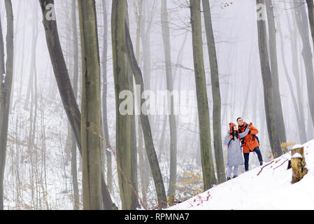 Paar Touristen stehen auf dem Berg und schauen auf die Bäume beim Gehen mit den Rucksäcken im Winter verschneite Wald Stockfoto
