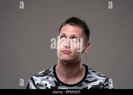 Junge Erwachsene gut aussehender Mann blickte nachdenklich Denken für eine Lösung auf grauem Hintergrund. Stockfoto