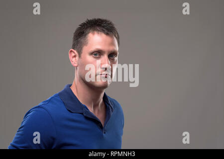 Moody Portrait von schweren selbstbewussten jungen Mann im blauen T-Shirt an Kamera suchen auf grauem Hintergrund. Stockfoto