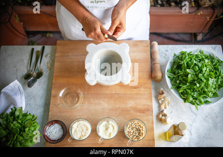 Eine Nahaufnahme der Hände eines weiblichen Chef hacken einige Knoblauch Pesto zu machen. Auf dem Tisch, alle anderen Zutaten. Stockfoto