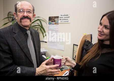 Junge Dame gibt eine Tasse heißen Getränk zu älteren Mann mit Sympathie und Lächeln, zeigt Respekt und kulturellen Verdienste der ukrainischen Gesellschaft, mann Pflege schätzt Stockfoto