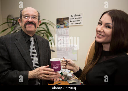 Junge Dame gibt eine Tasse heißen Getränk zu älteren Mann mit Sympathie und Lächeln, zeigt Respekt und kulturellen Verdienste der ukrainischen Gesellschaft, mann Pflege schätzt Stockfoto