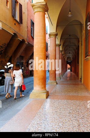 Mädchen, die an den Säulengängen in der Innenstadt von Bologna, Italien, vorbeilaufen. Bolognas Säulengänge gehören seit 2021 zum UNESCO-Weltkulturerbe Stockfoto