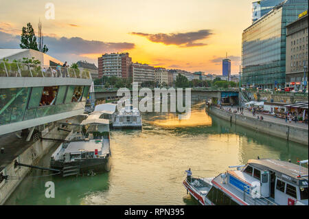 Riverboats und Cafés entlang des Donaukanals (Donaukanal) bei Sonnenuntergang, in der Nähe Schwedenplatz, Wien, Österreich Stockfoto