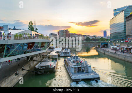 Riverboats und Cafés entlang des Donaukanals (Donaukanal) bei Sonnenuntergang, in der Nähe Schwedenplatz, Wien, Österreich Stockfoto