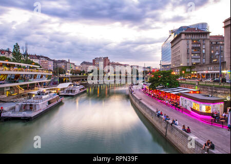 Riverboats und Cafés entlang des Donaukanals (Donaukanal) bei Sonnenuntergang, in der Nähe Schwedenplatz, Wien, Österreich Stockfoto