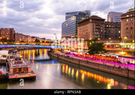 Riverboats und Cafés entlang des Donaukanals (Donaukanal) bei Sonnenuntergang, in der Nähe Schwedenplatz, Wien, Österreich Stockfoto