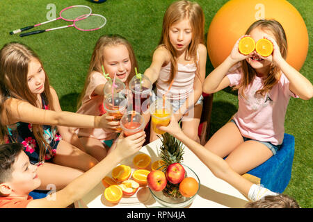 Kids Fashion Concept. Die Gruppe der jugendlich Jungen und Mädchen sitzen auf grünem Gras im Park. Kinder bunte Kleidung, Lifestyle, trendigen Farben Konzepte. Stockfoto