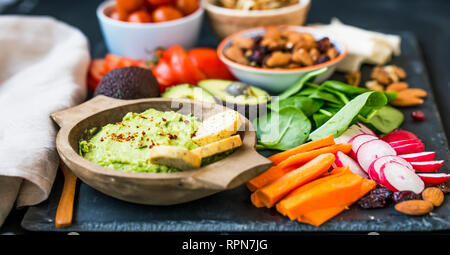Gesundes Essen auswahl mit Guacamole, rohes Gemüse, grüne Blätter spinat, Kräuter und Zutaten, Mischung von Nüssen, sauber essen, gesunde vegane Ernährung anhand von quantitativen Simulatio Stockfoto