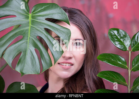 Nahaufnahme, Porträt einer jungen Brünette Dame. Das Girl posiert, entfernt. Green Palm Blätter Surround ihr Gesicht Stockfoto