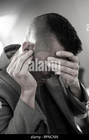 Nahaufnahme eines Leidens kaukasischen Mann mit einer Hand in seinem Kopf und mit der anderen Hand über sein Ohr Stockfoto