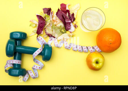 Hanteln für Sport. Fitness Salat und Maßband auf einem gelben Tabelle. Orangen, Äpfel und klares Wasser mit Eis für das Konzept einer gesunden lifestyl Stockfoto