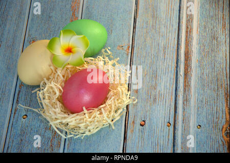 Drei Ostereier mit dekorativen Kugeln und eine Blume liegen auf dem Stroh auf einen hölzernen Tisch. Close-up. Stockfoto