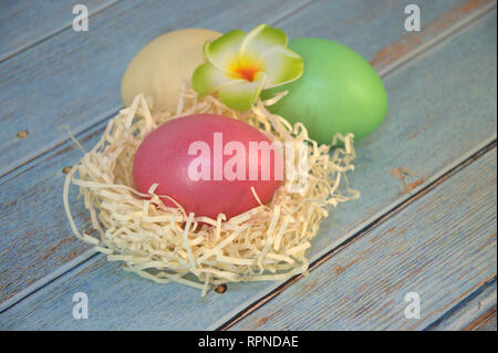 Drei Ostereier mit dekorativen Kugeln und eine Blume liegen auf dem Stroh auf einen hölzernen Tisch. Close-up. Stockfoto