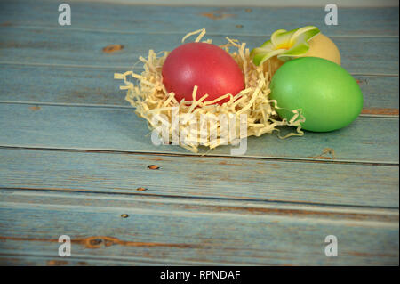 Drei Ostereier mit dekorativen Kugeln und eine Blume liegen auf dem Stroh auf einen hölzernen Tisch. Close-up. Stockfoto