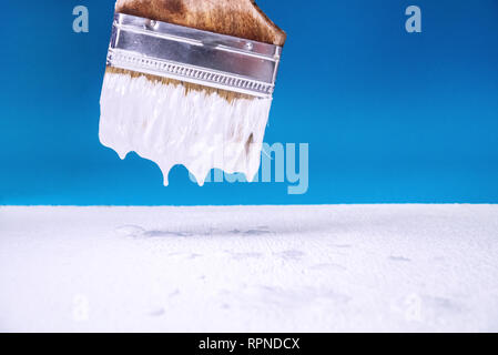 Mit einem Pinsel tropft weiße Farbe auf der Oberfläche der Malerei. blauen Hintergrund. Stockfoto