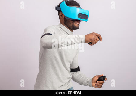 Dunkelhäutige zuversichtlich, dass man mit einer kurzen Stoppeln, pullower in Weiß gekleidet, trägt blaue mobile virtual reality Headset halten sich an den Händen, als ob Er fah Stockfoto