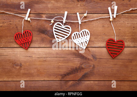 Valentines Tag romantischen Hintergrund, rote und weiße handgefertigten Holz Spielzeug dekorative Herzen hängen auf braune Holztisch, happy holiday am 14. Februar, dat Stockfoto