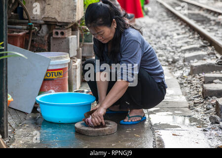 Lokale Frau vorbereiten und Schneiden von Fleisch auf eine hölzerne Tafel außerhalb ihrer Heimat und neben einer Bahntrasse, Hanoi, Vietnam, Asien Stockfoto