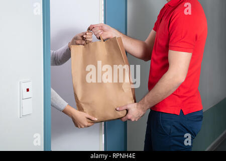 Ein junger hübscher Mann, der Papiertüte zu Frau zu Hause Stockfoto