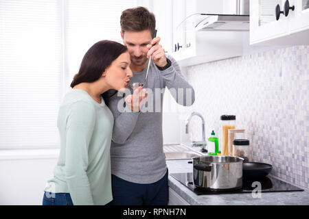 Junger Mann, der seine Frau schmeckt das Essen in der Küche zu Stockfoto