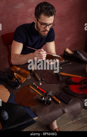 Junge Designer mit einer Bürste während in den schuhladen mit moderrn Innenraum arbeiten. Bis schließen Foto Stockfoto