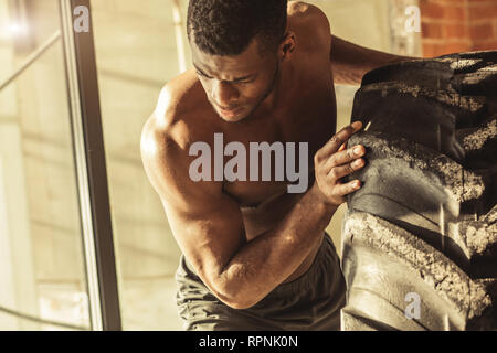 African American crossfit Mann bemüht sich zwar hart mit Hingabe und Entschlossenheit Anheben schwerer Reifen, Training von Kraft und Ausdauer Stockfoto