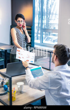 Aufmerksame brunette weibliche Person, die Papiere mit Diagrammen Stockfoto