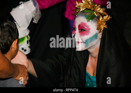 Eine schöne und liebevolle mexikanische Mädchen mit Schädel und Tracht lächelt und beruhigend ein trauriges Kind während der jährlichen Feier des Stockfoto