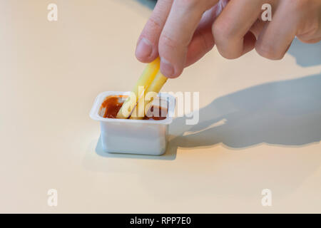 In der Nähe der weiblichen Hand tauchen Pommes in Tomatensoße. Hand mit frischen Pommes Frites tauchte in Tomatensauce. Vertikaler. kopieren. Stockfoto