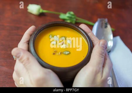 Schüssel mit warmem Kürbis Suppe in die Hände. Holding Schüssel vegane Kürbissuppe. Komfort Essen. Weibliche Hände. Stockfoto