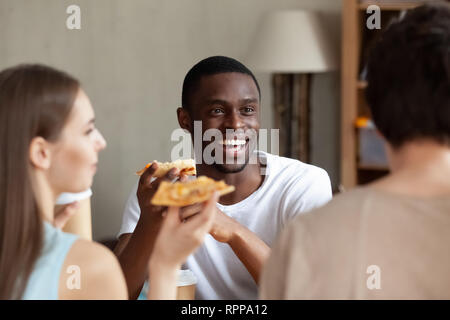 Lächelnd afrikanische amerikanische Mann essen Pizza, mit Freunden chatten Stockfoto
