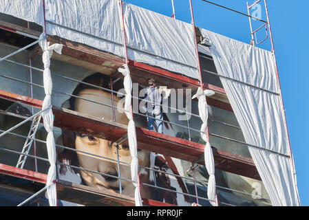 Berlin, Deutschland. 18 Feb, 2019. Der Künstler Tank schaut auf die Spezifikation einer Mona Lisa Ausdruck, um es so genau wie möglich auf die Fensterlosen Haus Fassade der East Side Hotel zu malen. Gemeinsam mit der Berliner Künstlergruppe Dixons sterben, er malt die übergroßen Mona Lisa auf der fensterlosen Fassade der East Side Hotel. Quelle: Annette Riedl/dpa/Alamy leben Nachrichten Stockfoto