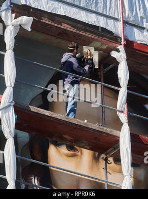 Berlin, Deutschland. 18 Feb, 2019. Der Künstler Tank schaut auf die Spezifikation einer Mona Lisa Ausdruck, um es so genau wie möglich auf die Fensterlosen Haus Fassade der East Side Hotel zu malen. Gemeinsam mit der Berliner Künstlergruppe Dixons sterben, er malt die übergroßen Mona Lisa auf der fensterlosen Fassade der East Side Hotel. Quelle: Annette Riedl/dpa/Alamy leben Nachrichten Stockfoto