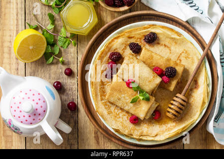 Gesunde Pfannkuchen Frühstück. Stapel von hausgemachten dünne Pfannkuchen oder Crepes auf einer rustikalen Tisch, mit Honig und frischen Beeren serviert. Ansicht von oben flach backgr Stockfoto