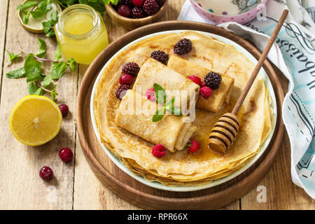Gesunde Pfannkuchen Frühstück. Stapel von hausgemachten dünne Pfannkuchen oder Crepes auf einer rustikalen Tisch, mit Honig und frischen Beeren serviert. Stockfoto